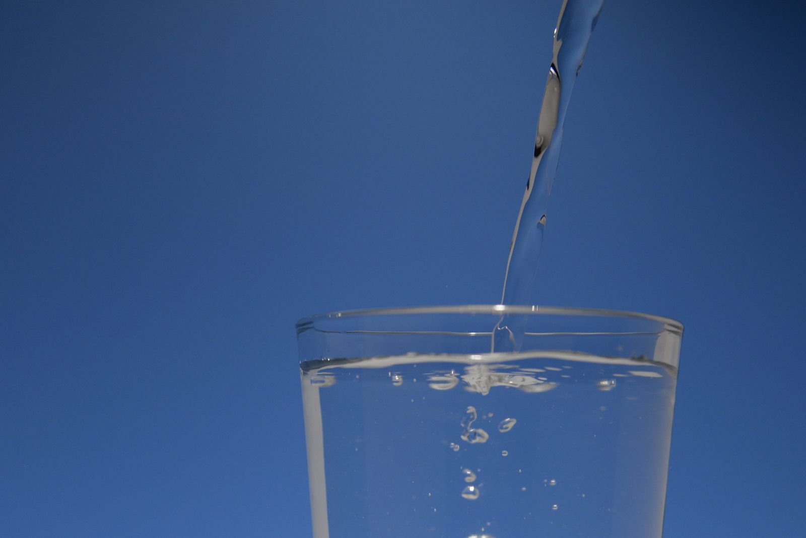 Klares Trinkwasser fliesst in ein Glas vor blauem Hintergrund